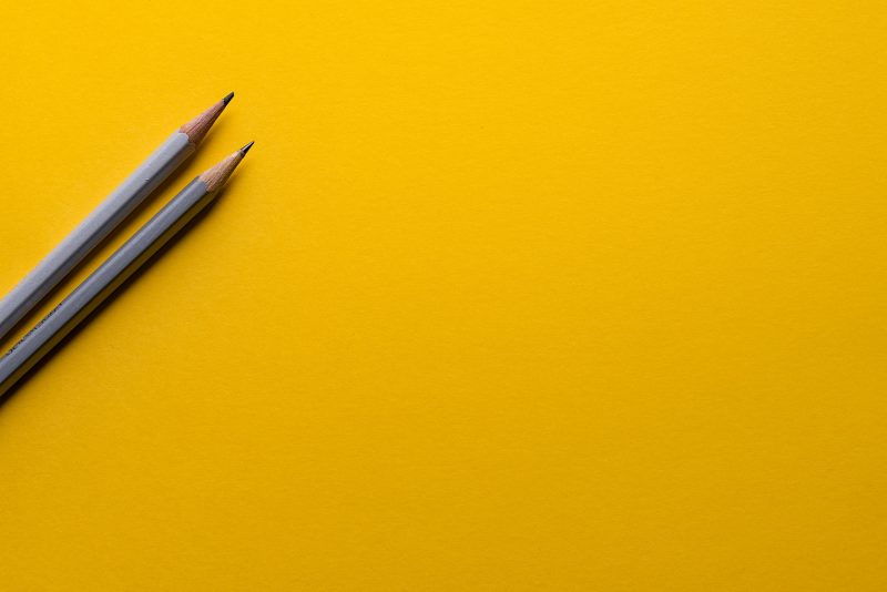 Two pencils lay on a bright yellow background